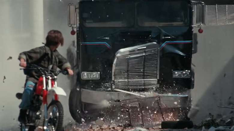 A still from the chase scene in Terminator 2: Judgment Day featuring Edward Furlong's John Connor on a dirtbike in the foreground, pursued by the T-100 in a big rig.