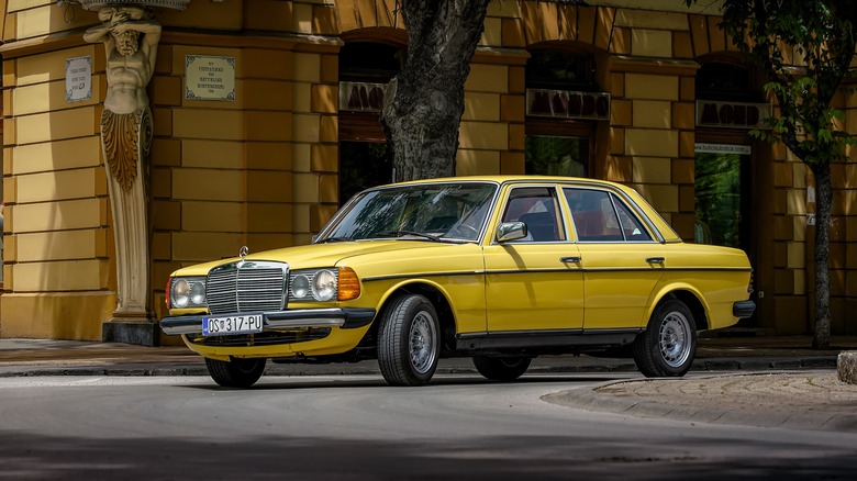 A W123 Mercedes in yellow taking a corner, front 3/4 view