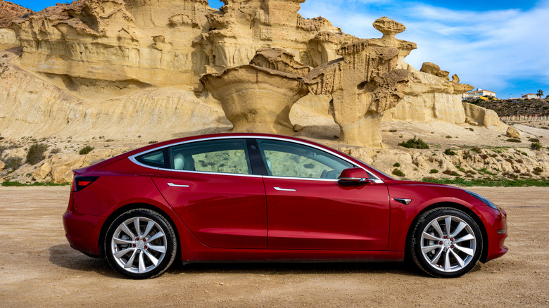 Red Tesla Model 3 parked in front of rock formation