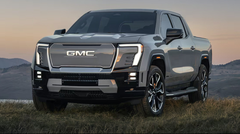 A gray GMC Sierra EV truck on a grassy hill at sunset