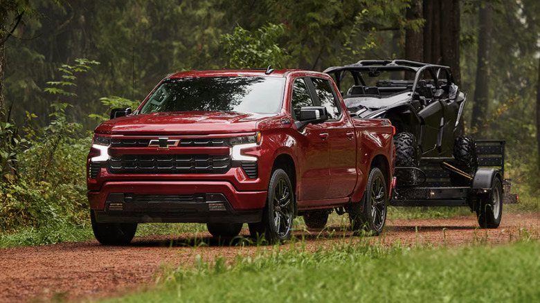 A red Chevy Silverado towing an ATV in the woods