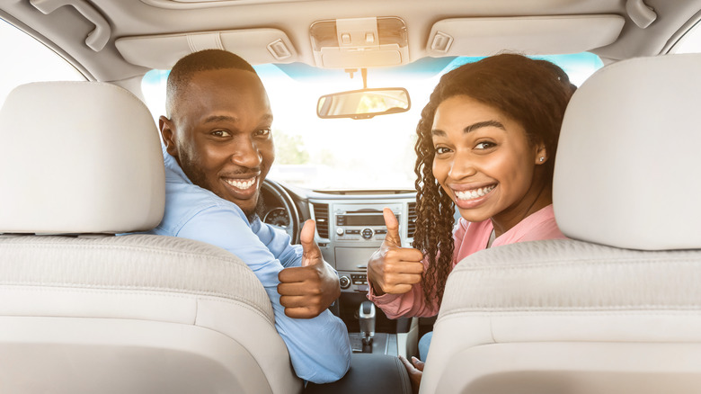 man and woman giving thumbs up in front seat