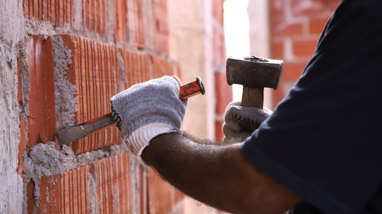 Hammer and chisel being used to remove mortar from brick wall