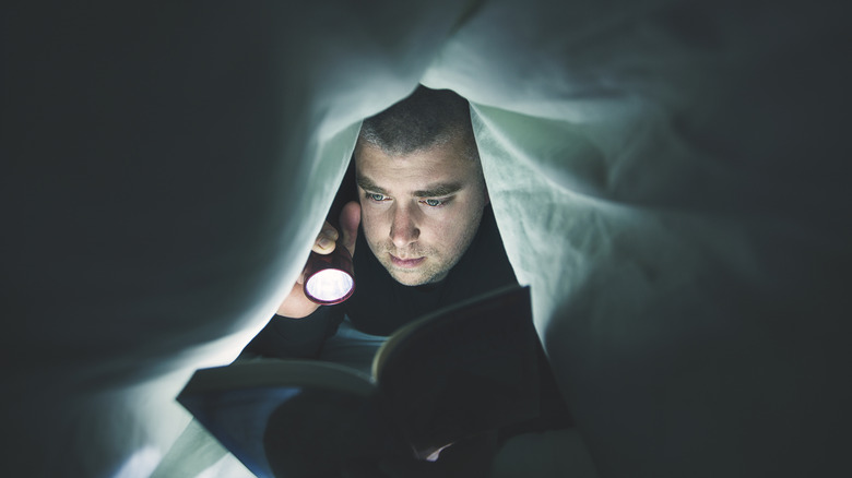 Man using a flashlight to read under the sheets