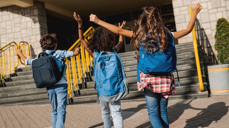 Children wearing backpacks entering a school