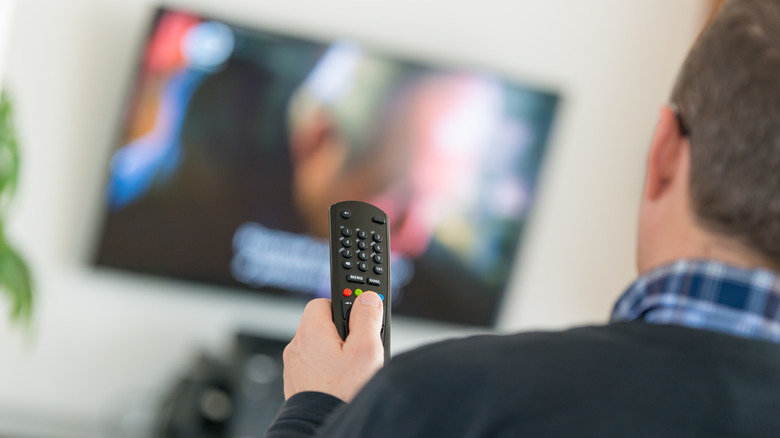Man holding remote pointed at TV.