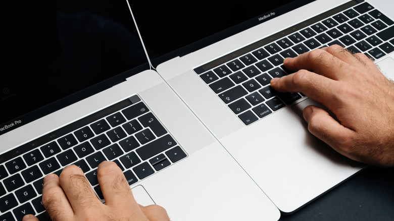 Person typing on two MacBook Pro laptops