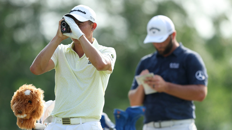 Golfer uses rangefinder to measure distance on course