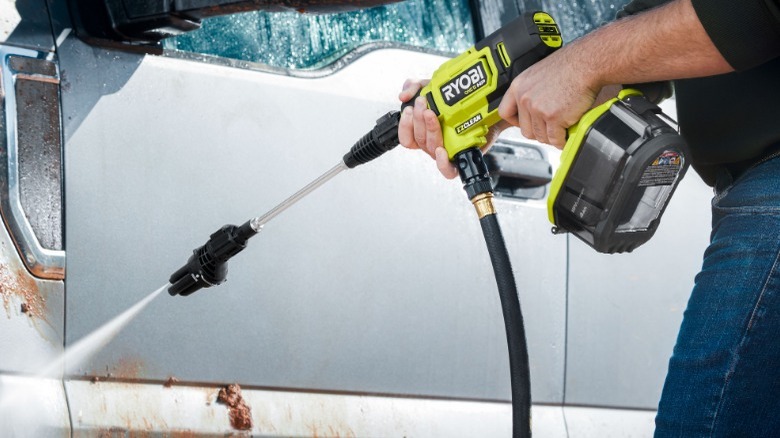 Person using pressure washer on car