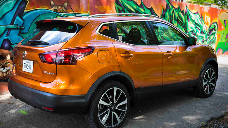 An orange Nissan Rogue Sport next to a wall with graffiti