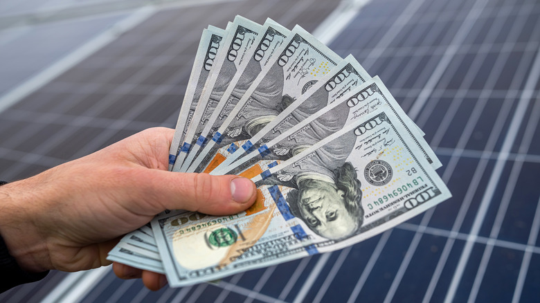 Hand holding cash with solar panels