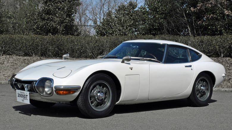 White Toyota 2000GT parked on an empty parking lot front 3/4 view