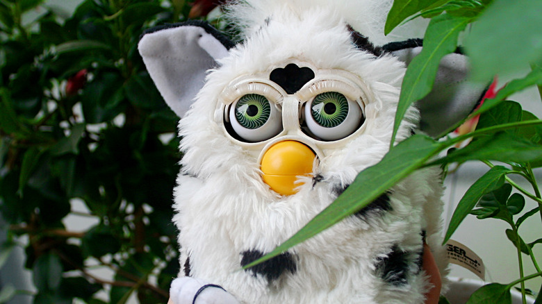Furby staring from behind a plant