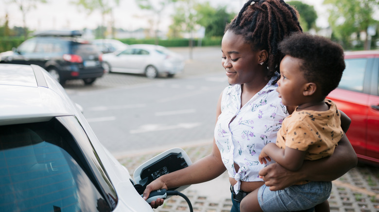 person charging electric vehicle holding child