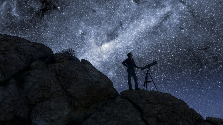 person with a telescope before a starry sky