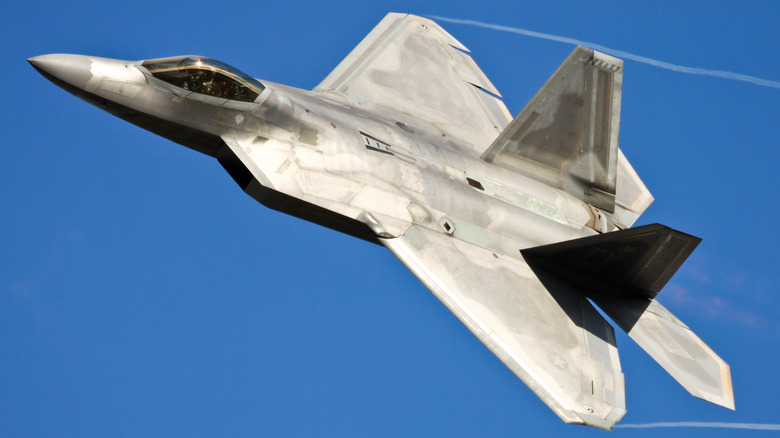 An F-22 Raptor fighter jet flying fast on a sunny morning.