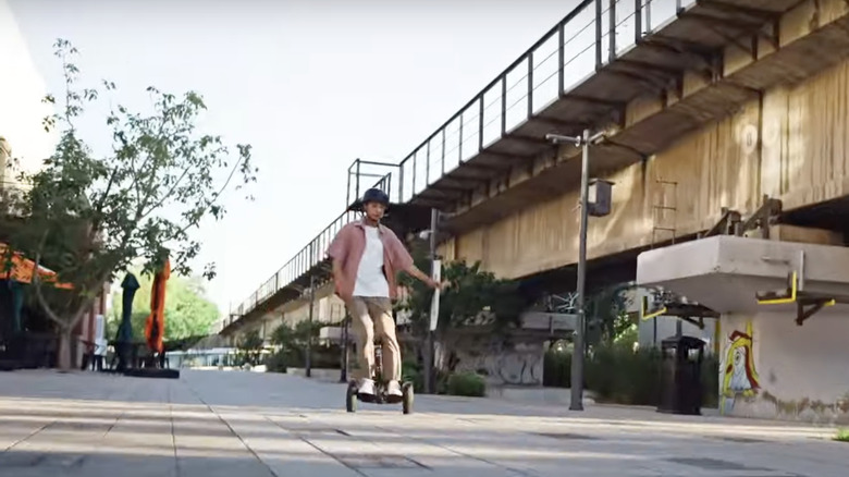 Young man riding Segway S2 scooter on city walkway in front of bridge