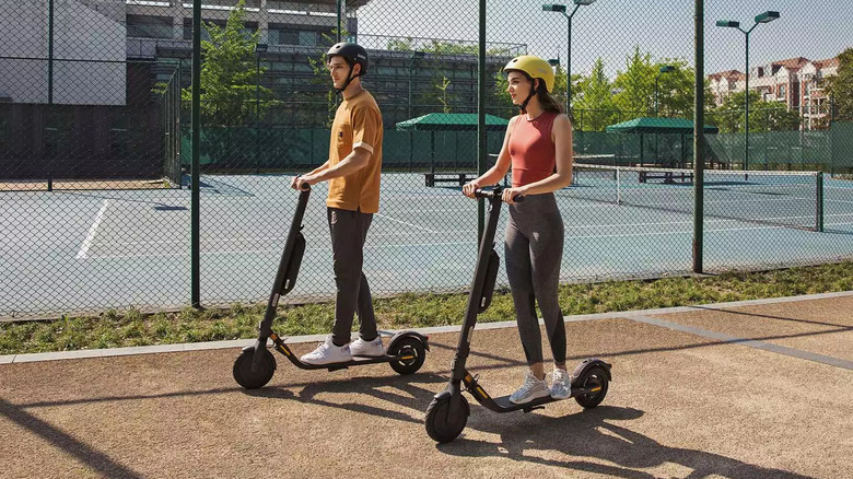 Couple riding side-by-side on Segway E45 scooters in front of tennis court