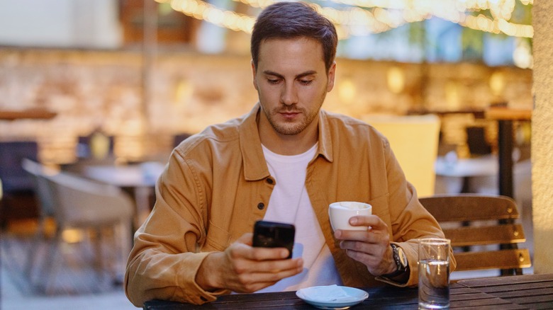 man using iphone drinking coffee