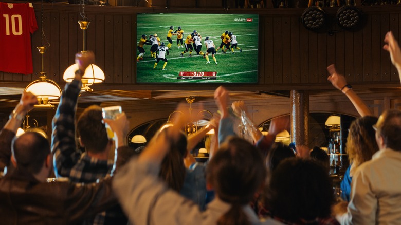 Fans cheering while watching an American football game at a pub