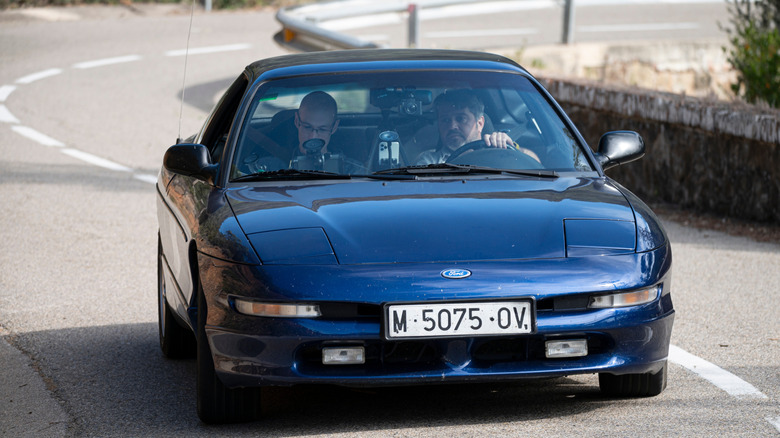 Men driving blue Ford Probe down road