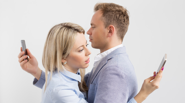 Two people embrace while looking at their iPhones