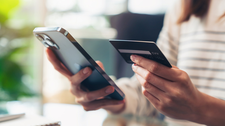 A person holding an iPhone in one hand and a credit card in the other