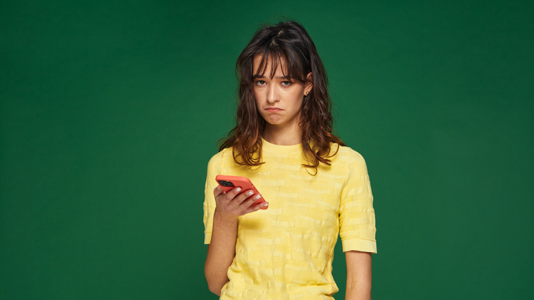 A girl uses an iPhone in a red case in front of a green background