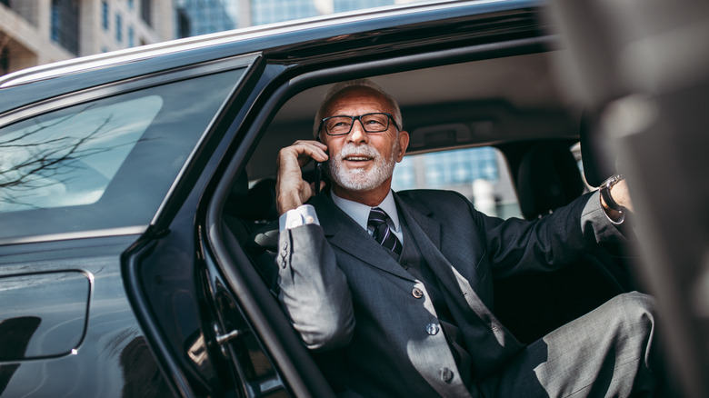 an older man in a luxury car holding a phone to his ear