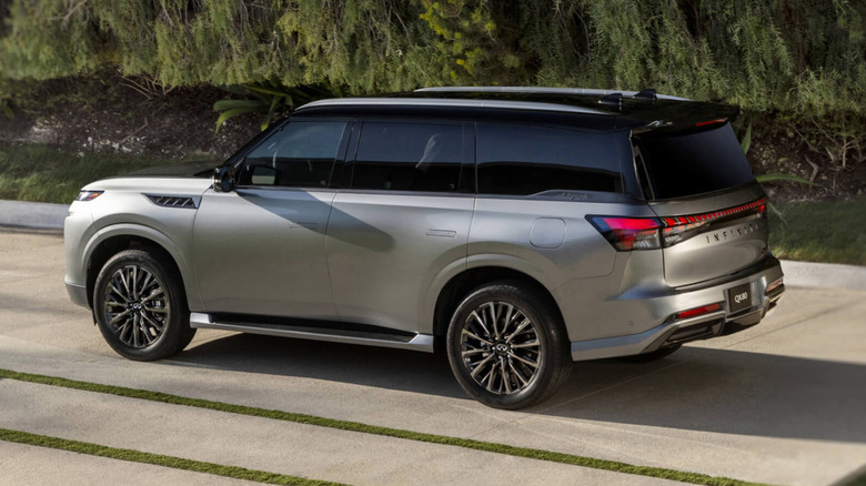 A gray Infinit QX80 in a grass-lined driveway