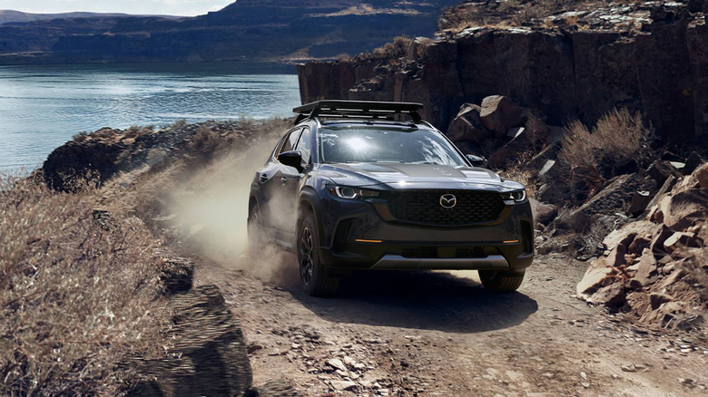 A Mazda CX-50 driving up a dirt path by a lake