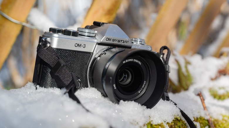 The OM System OM-3 camera with the M.ZUIKO 25mm f1.8 II lens sitting in the snow