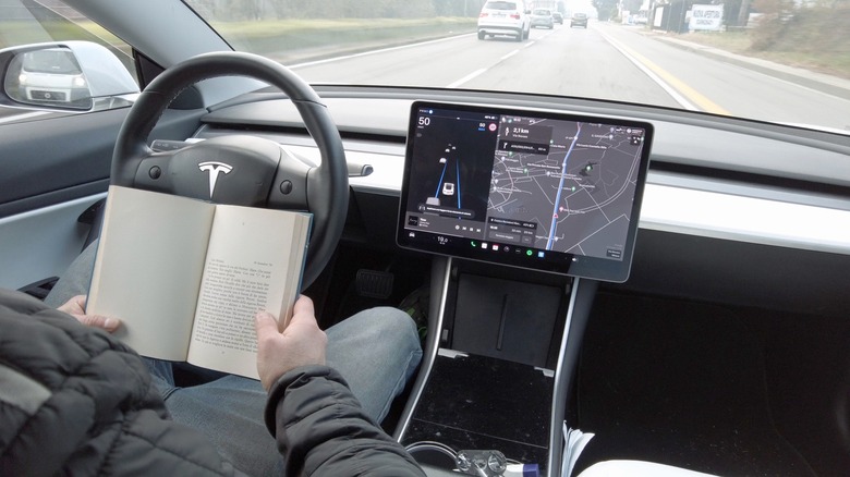 driver reading book in self-driving Tesla