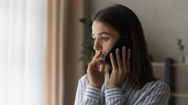 sad person looking out window while holding smartphone up to ear