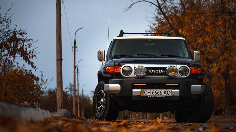 a black FJ Cruiser driving over autumn leaves