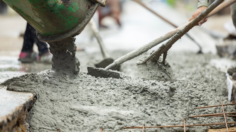 Cement pours from a cement truck spout, where it's shoveled by workers