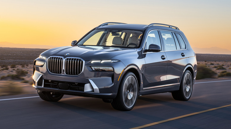 A BMW X7 driving on a road at sunset