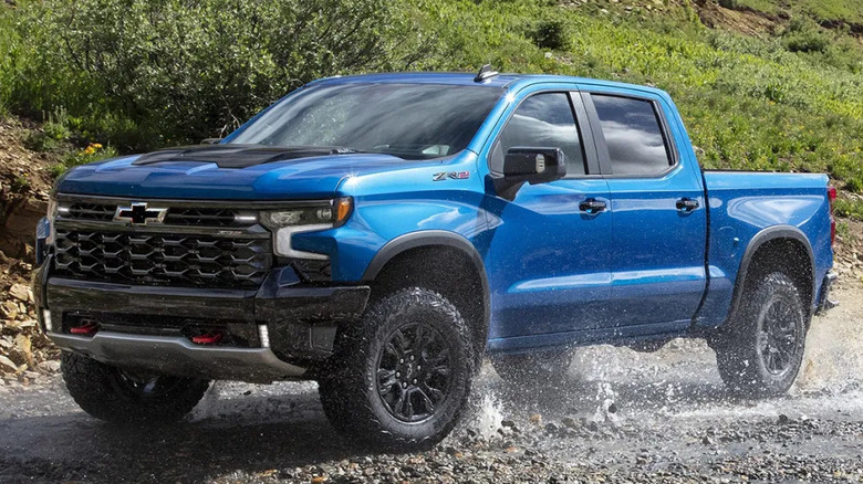 Blue Chevy Silverado driving through rocky wet terrain