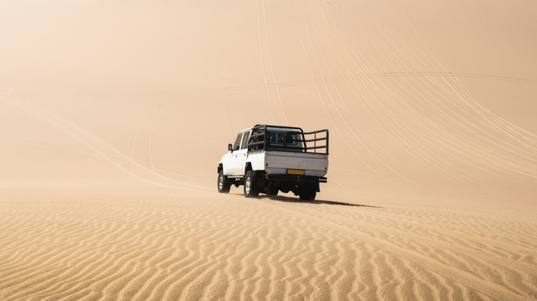 Older white truck driving on a sand dune