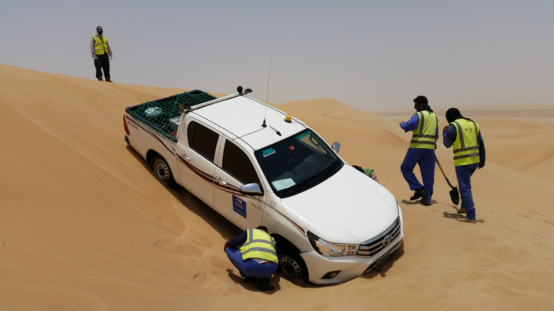 truck stuck in a sand dune with workers trying to dig it out