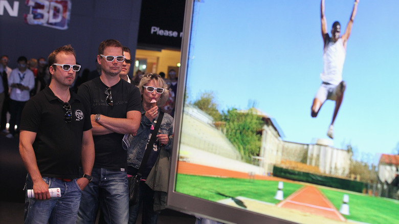 Visitors at a tech expo watch a 3D TV