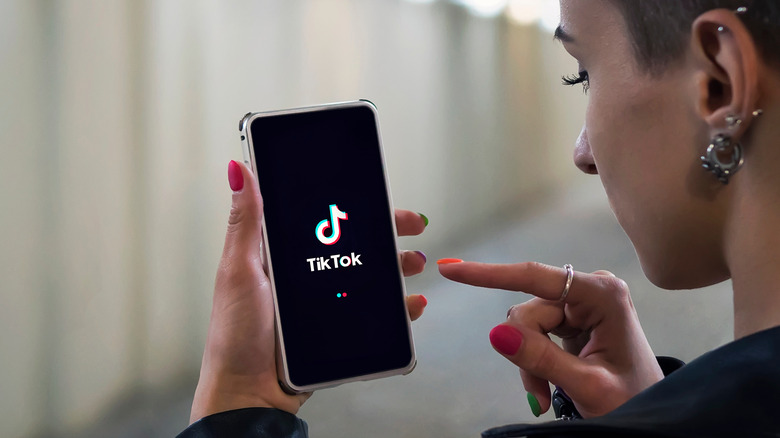 Woman holding phone displaying TikTok logo.