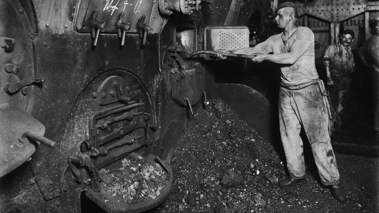 Man scoops coal in ship boiler room