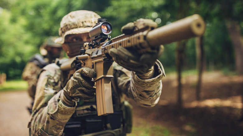 A soldier aims a rifle while walking.