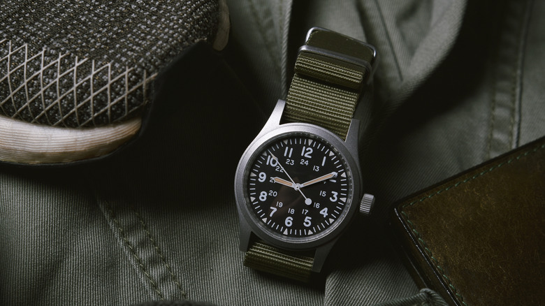 A watch with an olive drab band resting on military clothes.