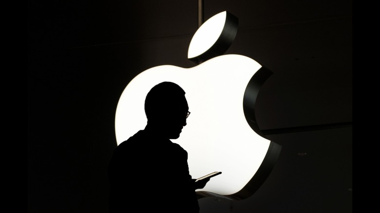 silhouette of a man using an iPhone in front of the Apple logo