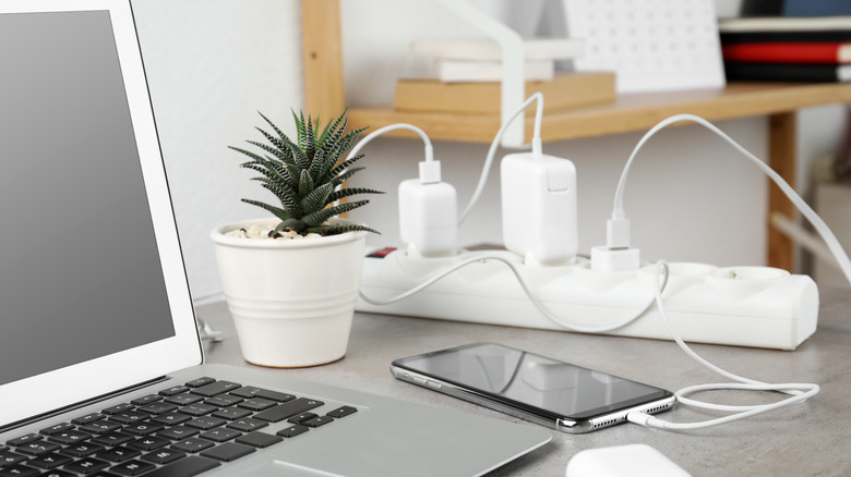 MacBook and smartphone on a table with charging bricks plugged into power strip