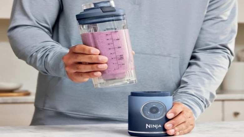 Person holding a blender cup with pink ingredients