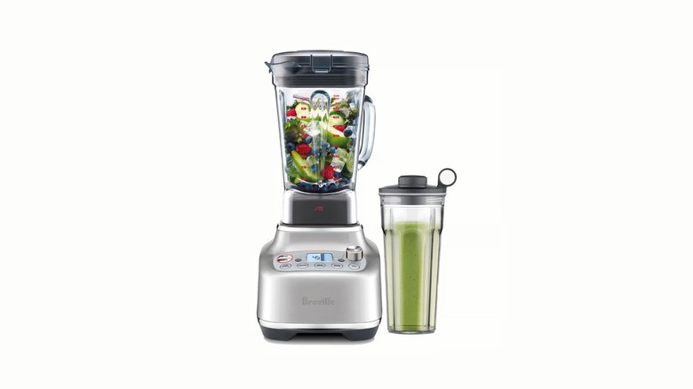 Silver blender base with pitcher containing unblended fruit and a matching cup with a green smoothie