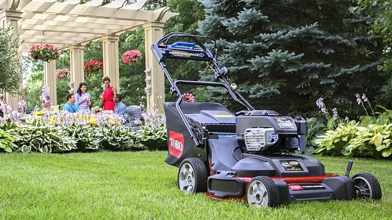 A Toro gas-powered lawn mower with a garden party in the background.